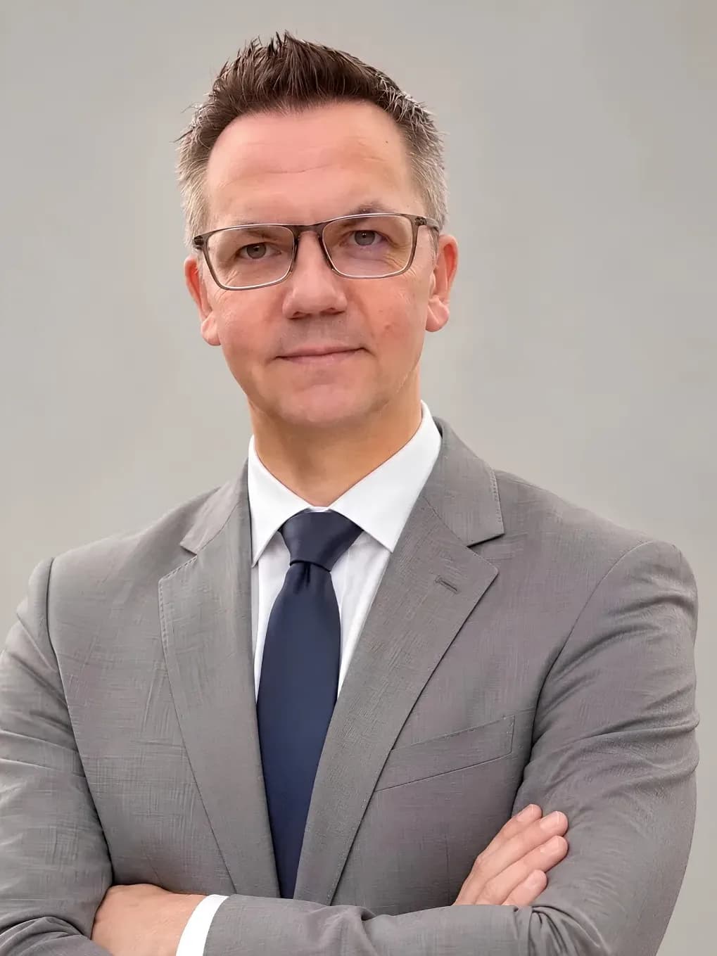 Matthias Schwier, Porträt im hellgrauen Anzug mit Krawatte vor hellem Hintergrund, KI-generiert mit Kennzeichnung