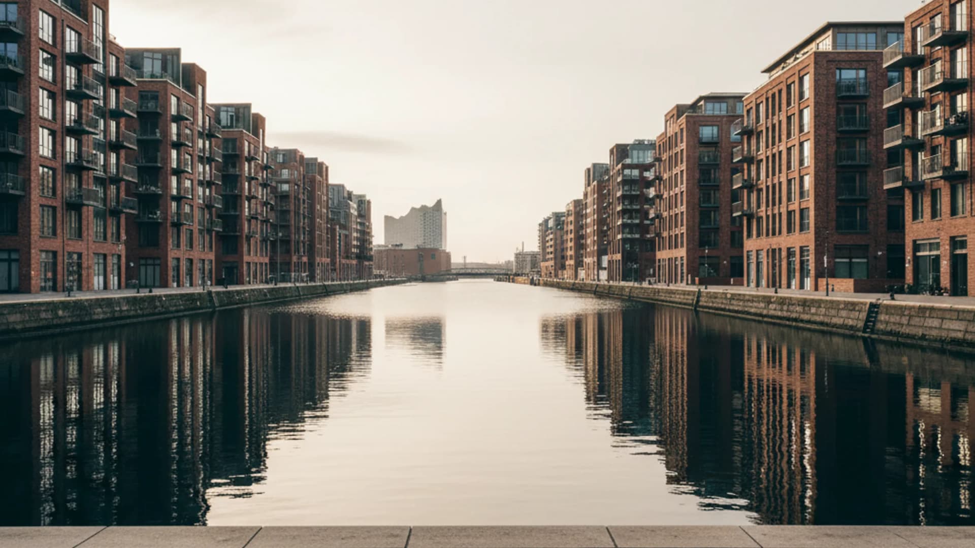 Backstein- und Glasarchitektur an einem Hafenbecken der Hamburger HafenCity mit Elbphilharmonie in der Distanz